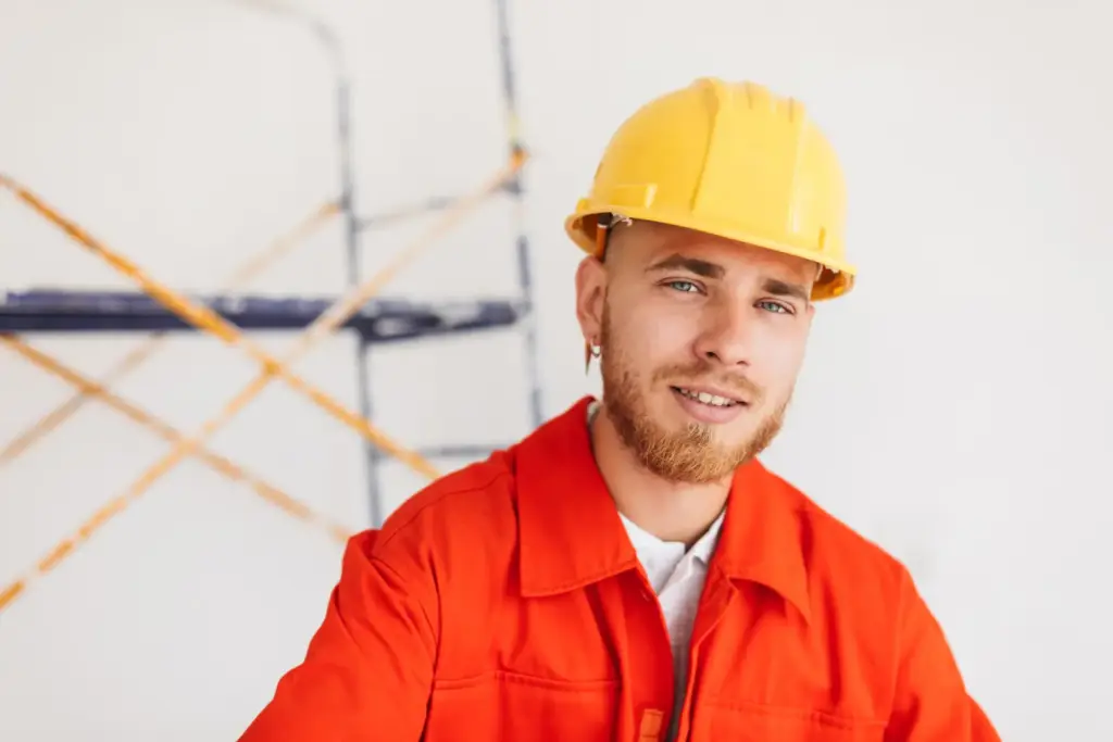 Uśmiechnięty budowlaniec w żółtym kasku i pomarańczowym ubraniu roboczym