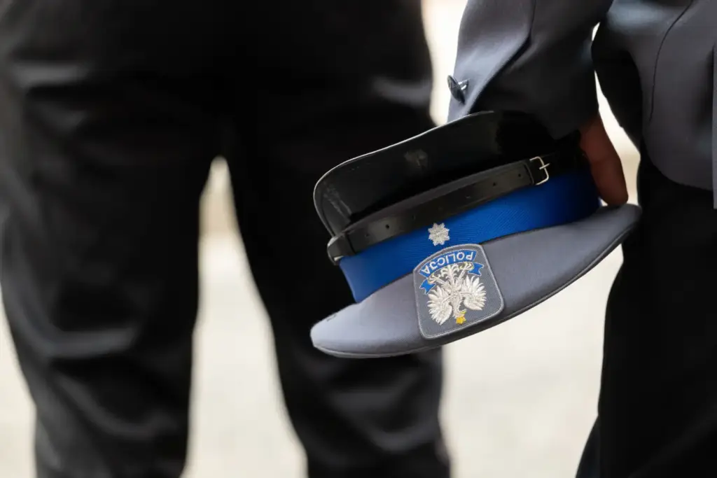 Policjant trzyma czapkę służbową z orłem i napisem Policja