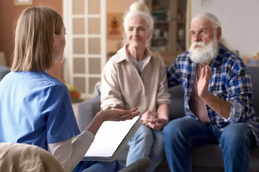 Pracownica socjalna z tabletem rozmawia z parą seniorów w ich domu