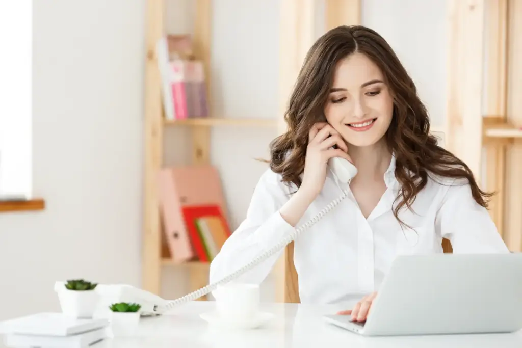 Uśmiechnięta sekretarka rozmawia przez telefon przy biurku