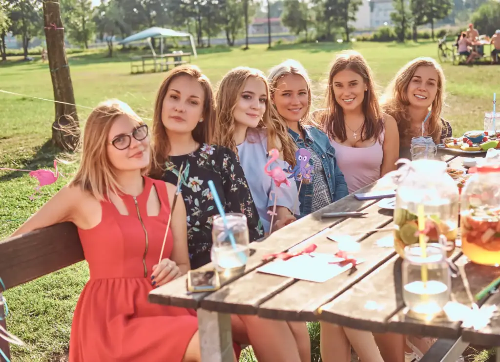 Grupa młodych kobiet przy stole w ogrodzie, z napojami i przekąskami, w letni dzień