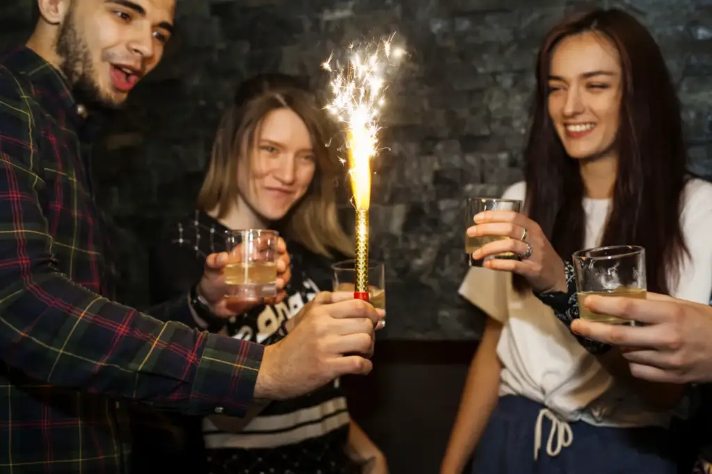 Młody mężczyzna z zimnym ogniem w dłoni wznosi toast w gronie przyjaciół