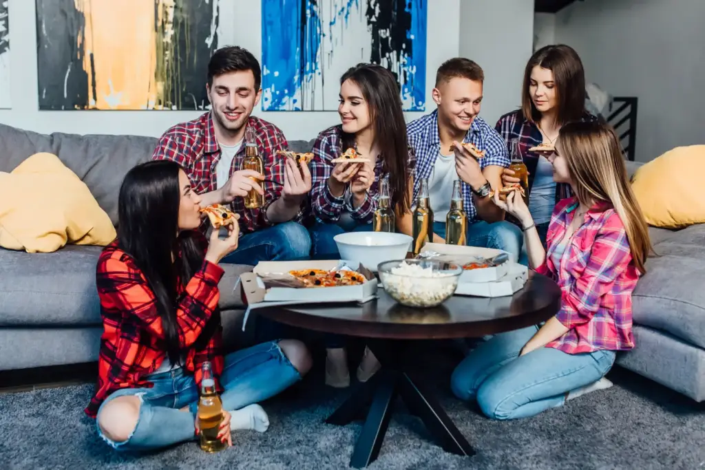 Młodzi ludzie przy stoliku z pizzą podczas domowej imprezy