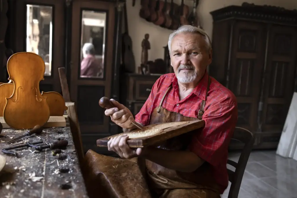 Siwy mężczyzna w warsztacie stolarskim trzyma w rękach drewniany element