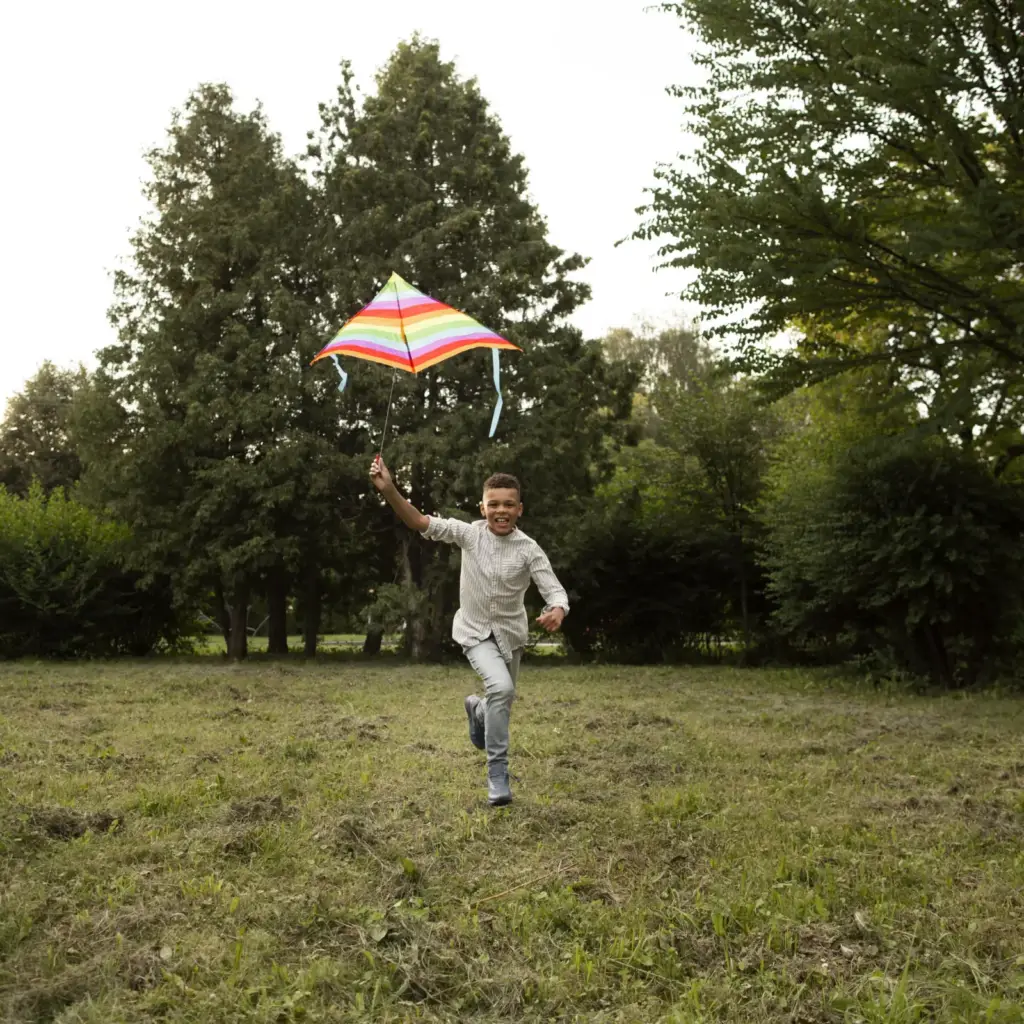 Chłopiec biegnie po łące z kolorowym latawcem